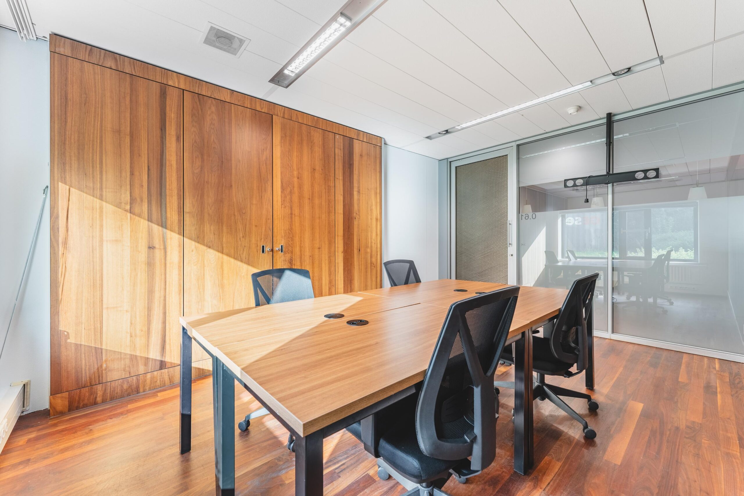 Vergaderruimte met houten vloer, grote houten kast, glazen wand en zes zwarte bureaustoelen rond een rechthoekige tafel op de Prof. W.H. Keesomlaan.